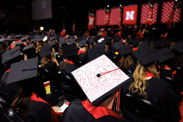 A graduate's mortarboard with children's signatures is seen among the seated graduates in Pinnacle Bank Arena.