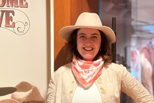 Student is wearing a cowboy hat and scarf standing in front of a Lonesome Dove poster.