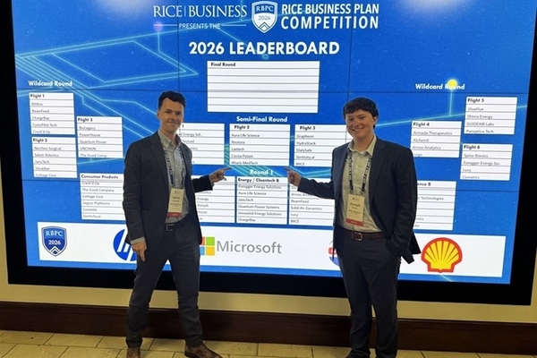 students stand in suits in front of a large screen showing a bracket for the competition. 