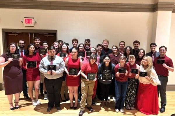 Students posing with trophies in conference room.