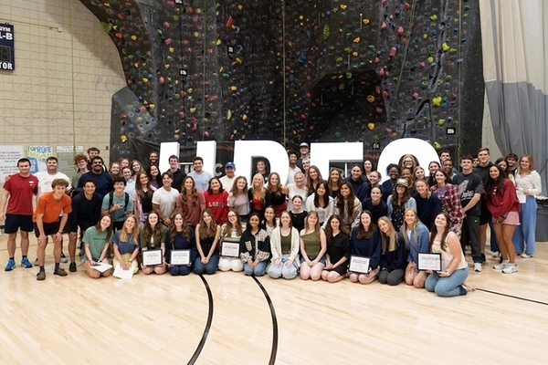 Students stand in group with awards in front of climbing wall. 