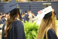 Two young women with long hairfrom the back, one with a decorated graduation cap.