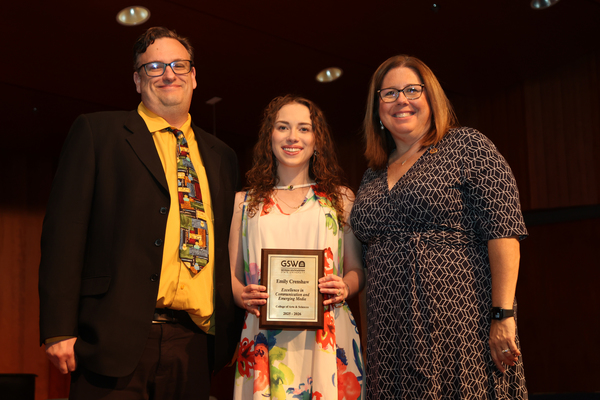 Student poses with plaque in between two faculty members