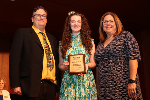 Student poses with plaque in between two faculty members