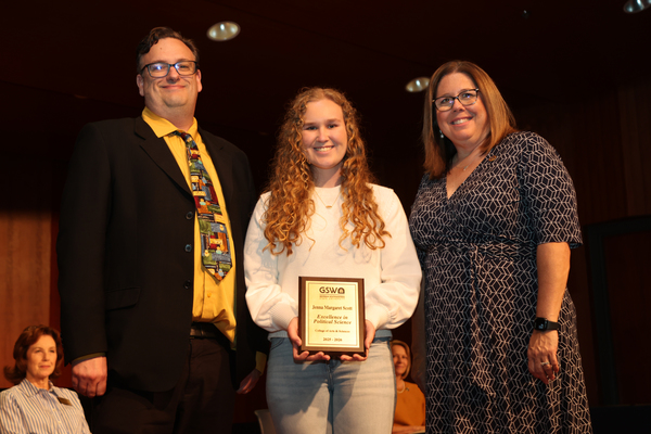 Student poses with plaque in between two faculty members