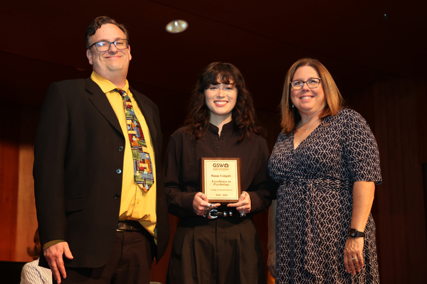 Student poses with plaque in between two faculty members