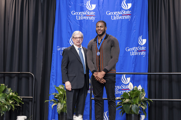 Dean Paul Alberto and award recipient Yamal Hilton pose for a photo on stage at the college's 2026 Scholars Recognition Luncheon.