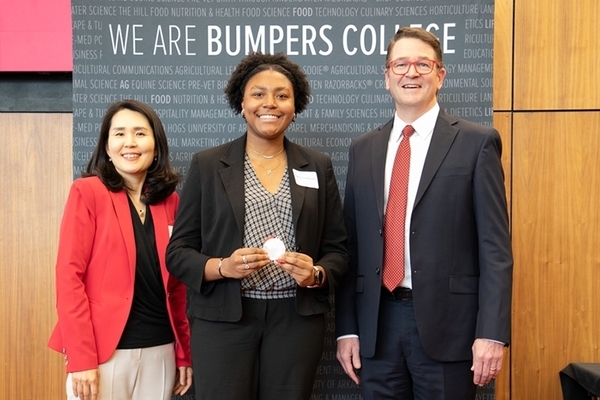 An honors students stands with a medal in front of a Bumpers College sign with two faculty members. 