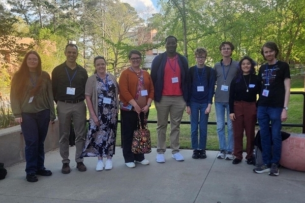 students standing in a group in front of trees at conference. 
