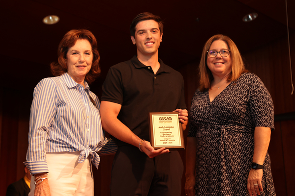 Student poses with plaque in between two faculty members