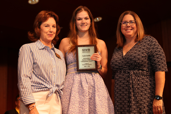 Student poses with plaque in between two faculty members