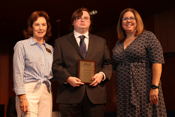 Student poses with plaque in between two faculty members