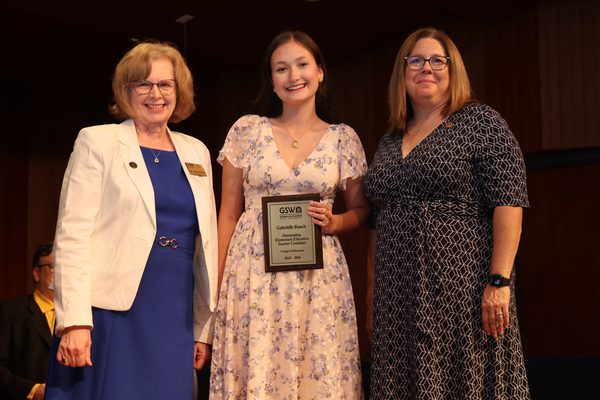 Student poses with plaque in between two faculty members