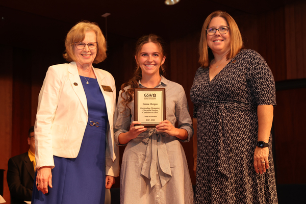 Student poses with plaque in between two faculty members