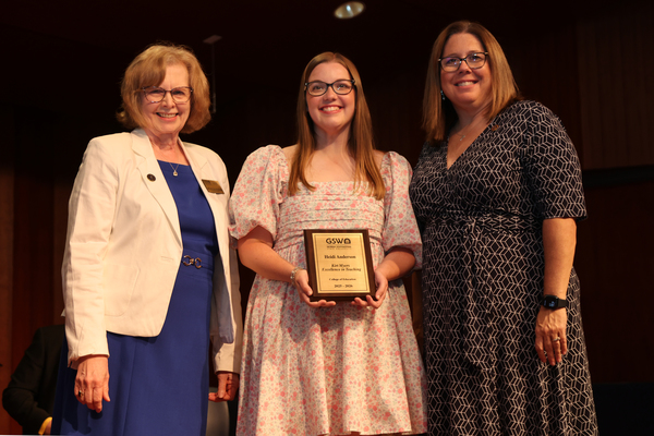 Student poses with plaque in between two faculty members