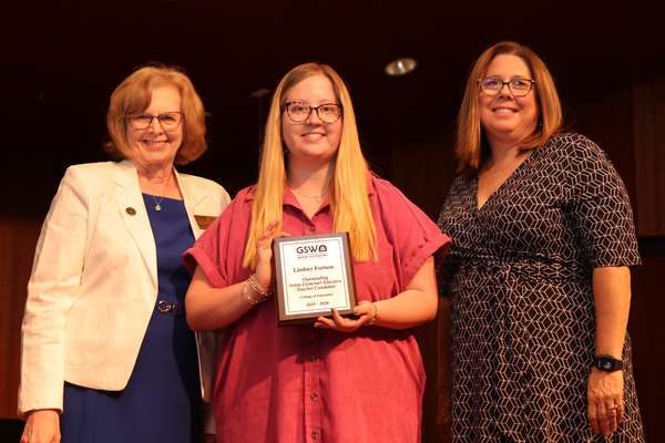 Student poses with plaque in between two faculty members