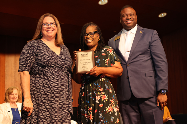 Student poses with plaque in between two faculty members