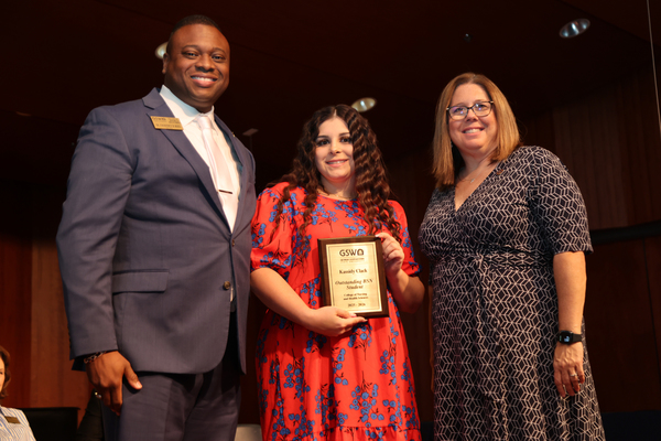 Student poses with plaque in between two faculty members