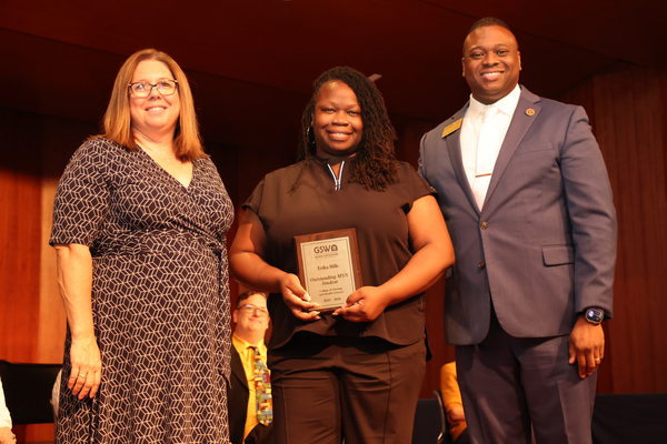 Student poses with plaque in between two faculty members