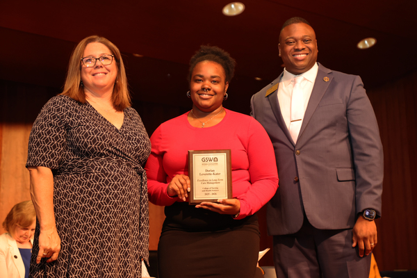 Student poses with plaque in between two faculty members