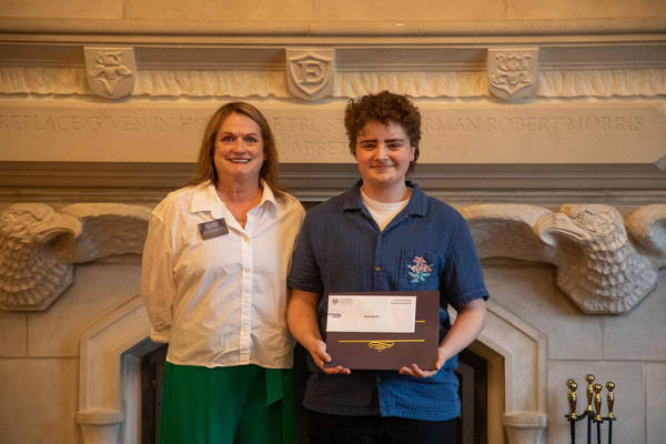 A woman with light-brown hair in a white top stands with a student with short curly hair and a blue polo shirt who is holding a certificate. 