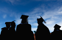 Graduates in shadow stand under a blue sky with wispy clouds.