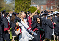 Jaidan Kertenis waves while wearing her Commencement robe and holding her mortarboard.