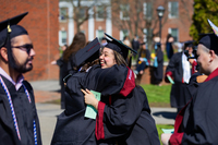 Two graduates hug while wearing their caps and gowns.