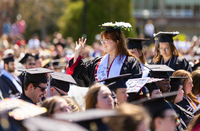 Rose Phillips waves while standing in a crowd of graduates at SUNY Potsdam. She has a decorated mortarboard with flowers.