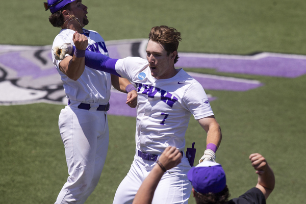 A college baseball player, jumping, being congratulated by teammates.