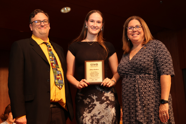 Student poses with plaque in between two faculty members