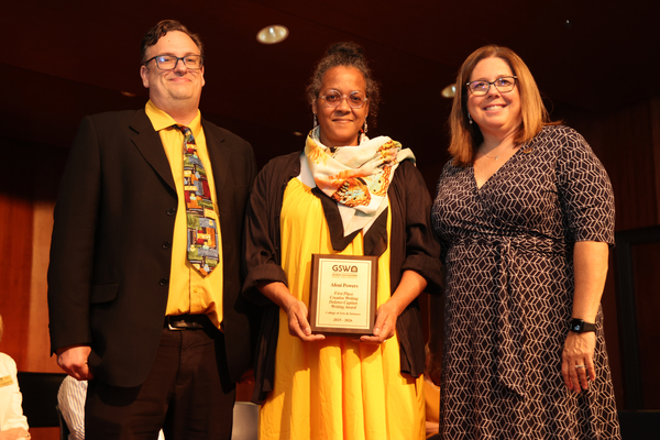 Student poses with plaque in between two faculty members
