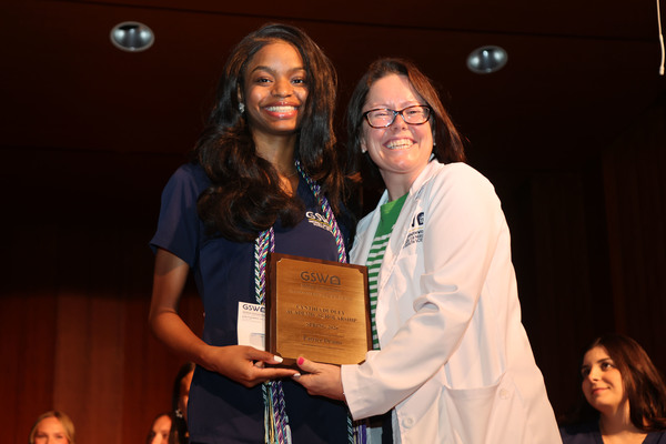 Student poses with plaque next to faculty member