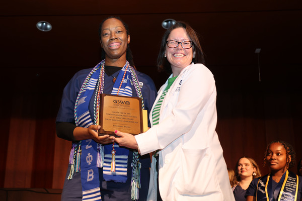 Student poses with plaque next to faculty member