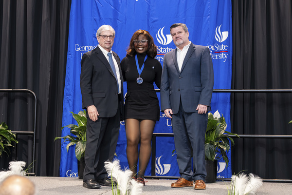 Paul Alberto, Ifedola Owoeye and Brendan Calandra pose for a photo on stage at the college's 2026 Scholars Recognition Luncheon.