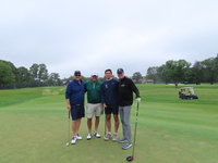 A group of 4 men standing on a golf course wearing golf gear