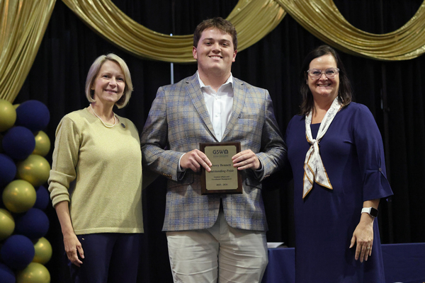 Student poses with plaque in between two staff members