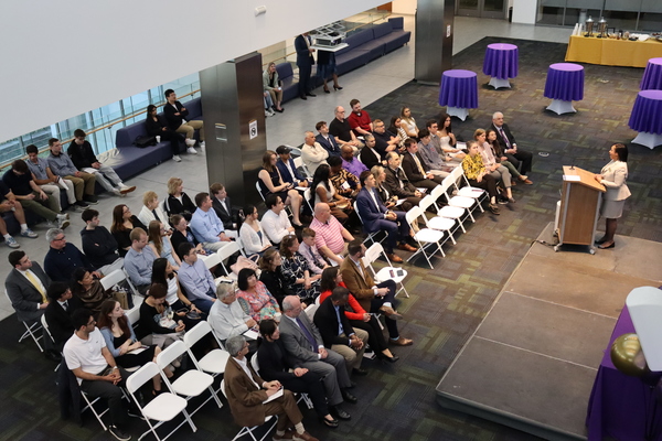 Three rows of an audience with a speaker standing at a podium.