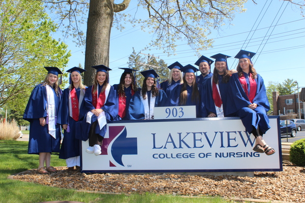 Students standing and sitting on the Lakeview College of Nursing sign outside of Lakeview College of Nursing's building. 