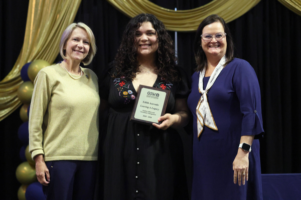 Student poses with plaque in between two staff members