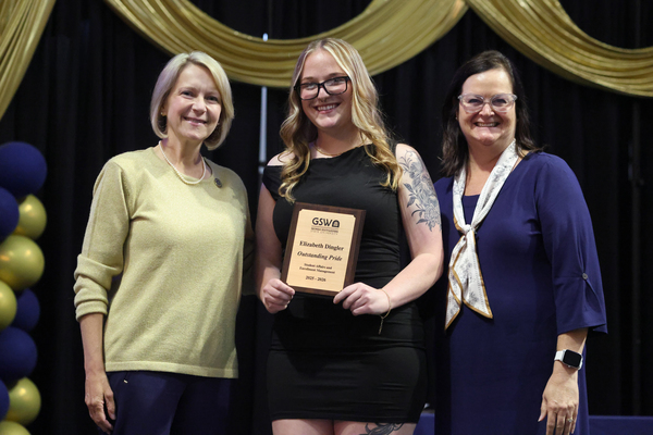 Student poses with plaque in between two staff members