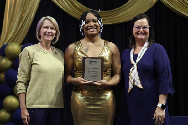 Student poses with plaque in between two staff members