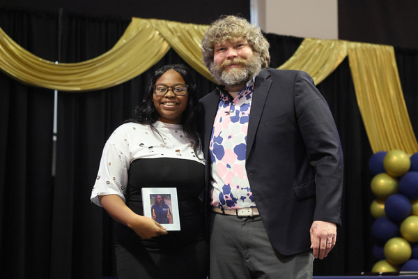 Student poses with plaque next to staff member