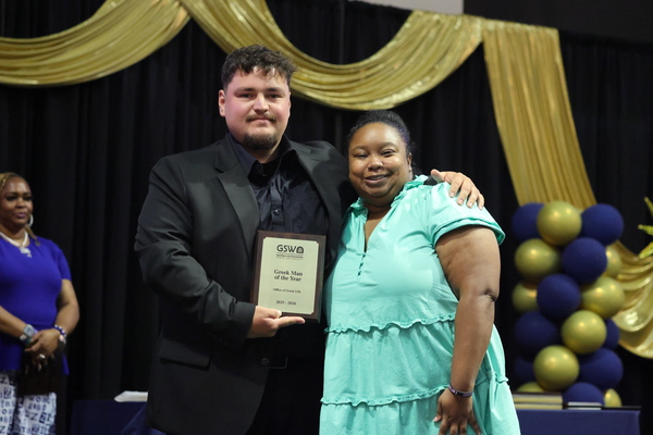 Student poses with plaque next to staff member