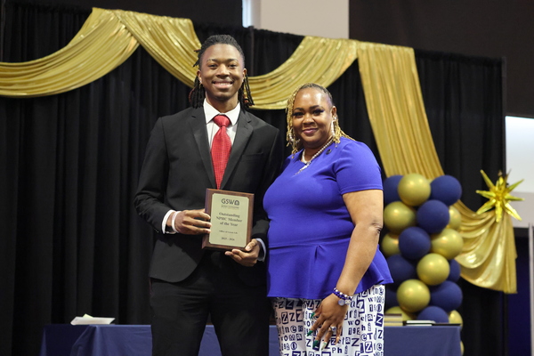 Student poses with plaque next to staff member