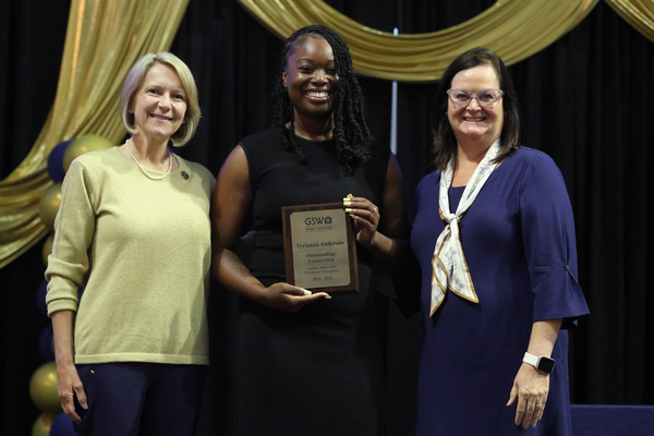 Student poses with plaque in between two staff members