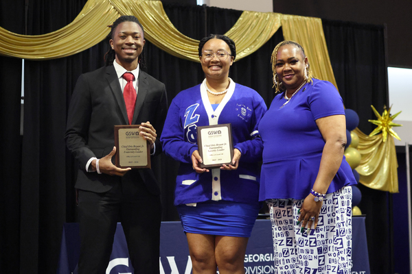 Students poses with plaque next to staff member