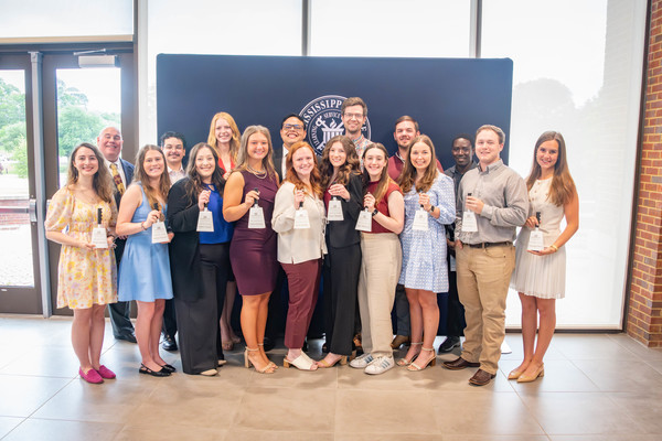 A group of students stand in front of a MSU seal and black background