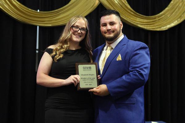 Student poses with plaque next to staff member