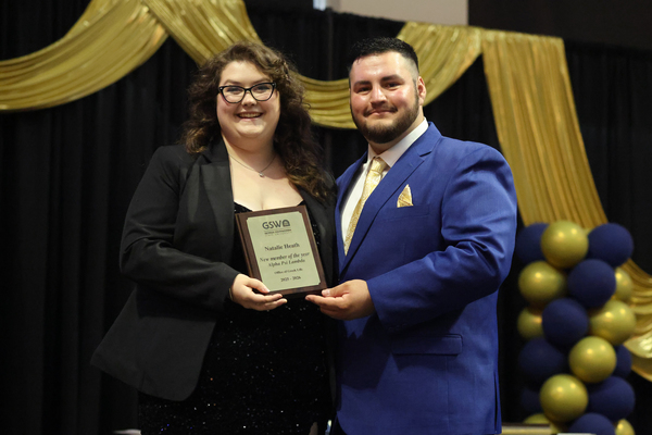 Student poses with plaque next to staff member